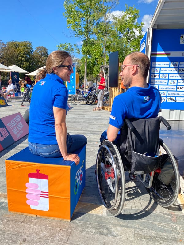 Eine Frau sitzt auf einem Hocker, ein Mann im Rollstuhl daneben. Sie unterhalten sich.